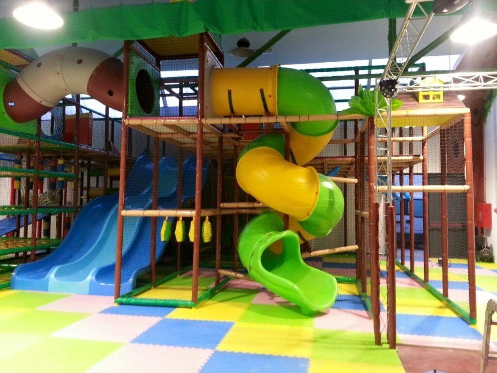 Parque de bolas con techo de hojas, toboganes en espiral y suelo de colores